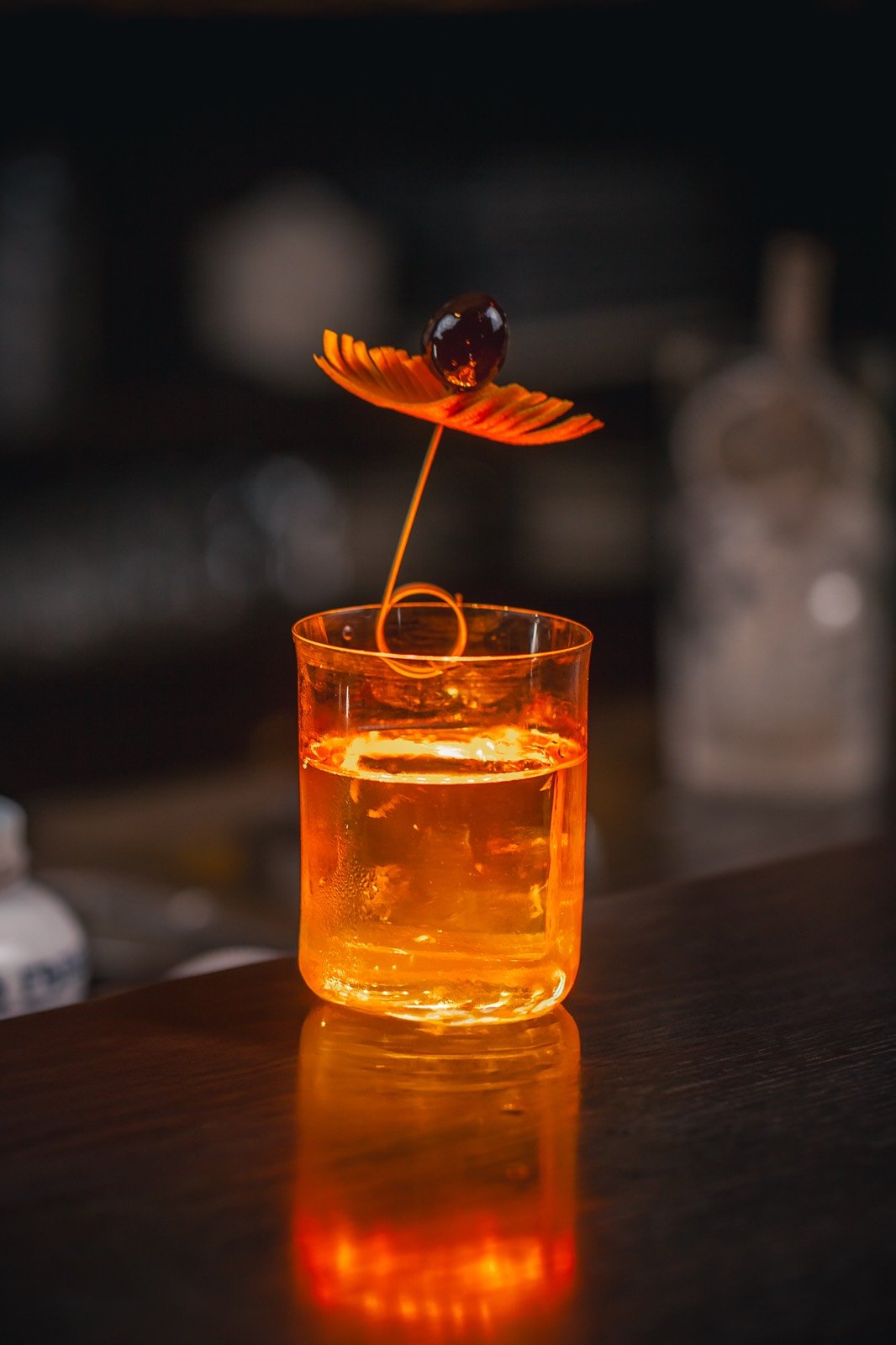 Un cocktail ambré, un zeste d’orange et une cerise, dans la lumière du comptoir